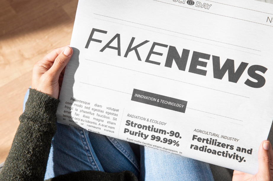 Person holding a newspaper with a bold “FAKE NEWS” headline.