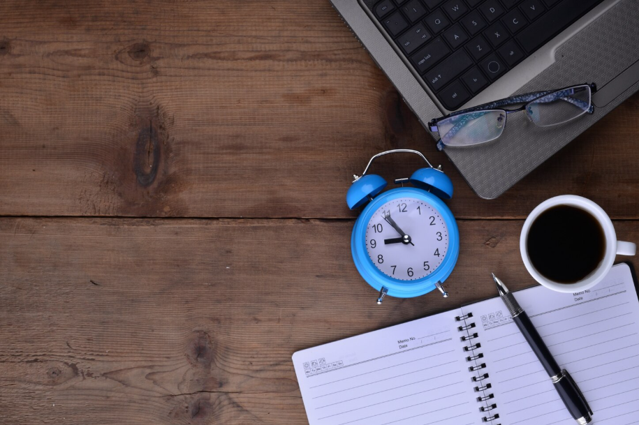 Overhead view of a desk with a blue alarm clock, open planner and pen, illustrating productivity and time management.