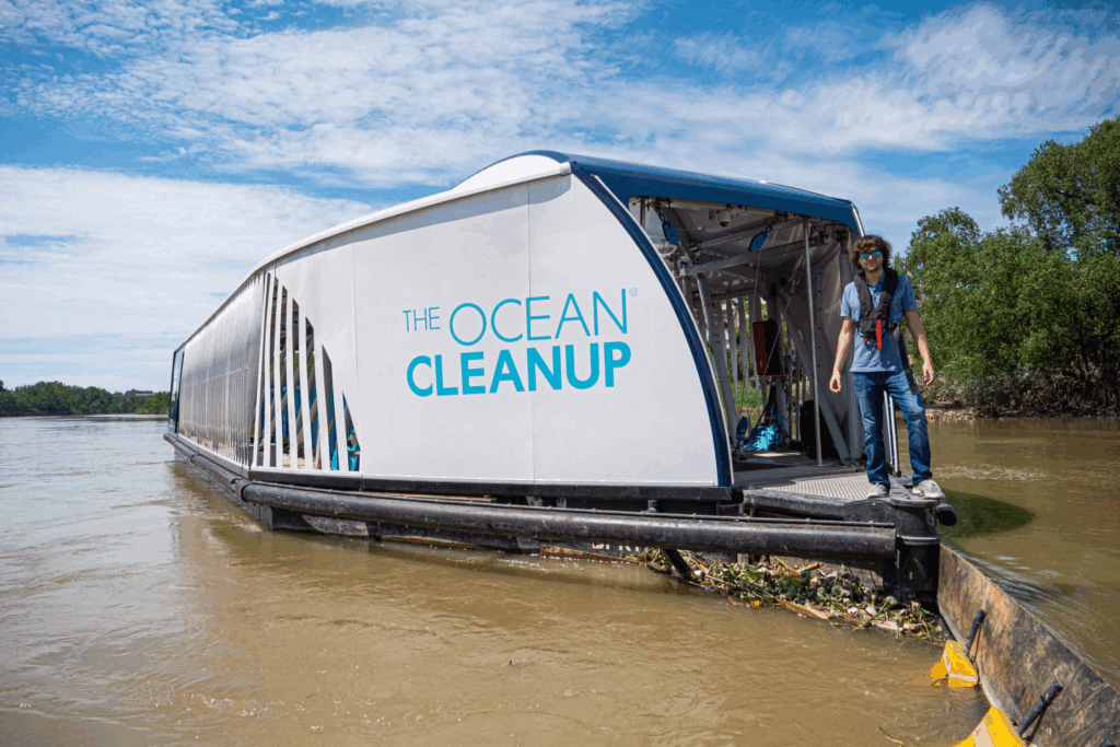 Solar-powered Ocean Cleanup Interceptor vessel collecting river plastic, with a crew member on deck.