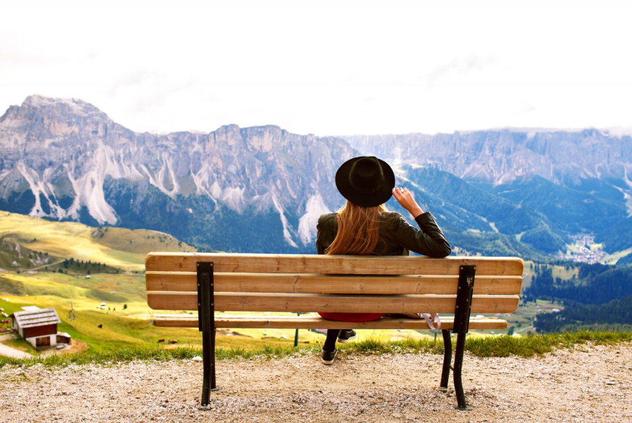Woman sitting alone on a bench overlooking peaceful alpine valleys and mountains.