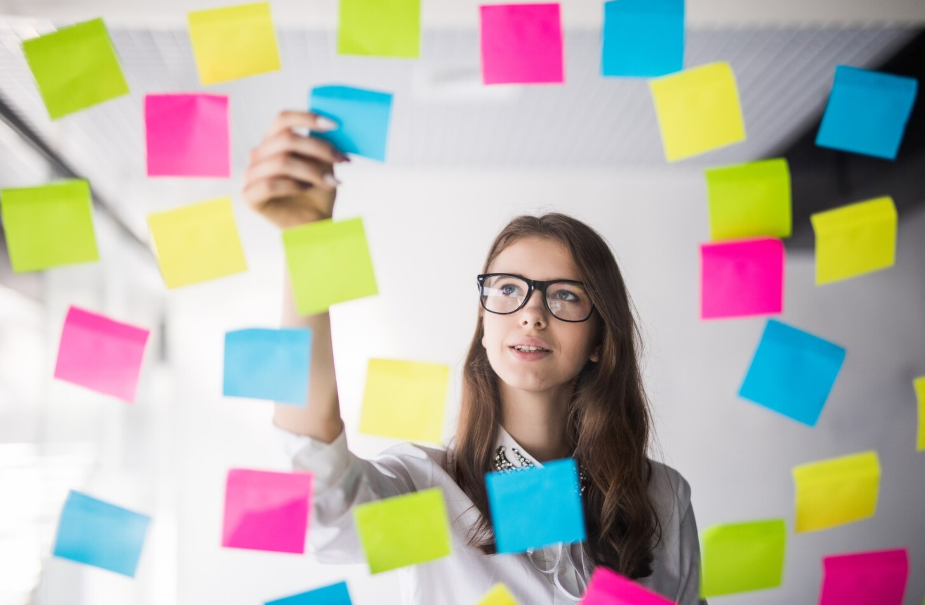 Woman organizing colorful sticky notes on a glass wall, illustrating techniques to train your memory.