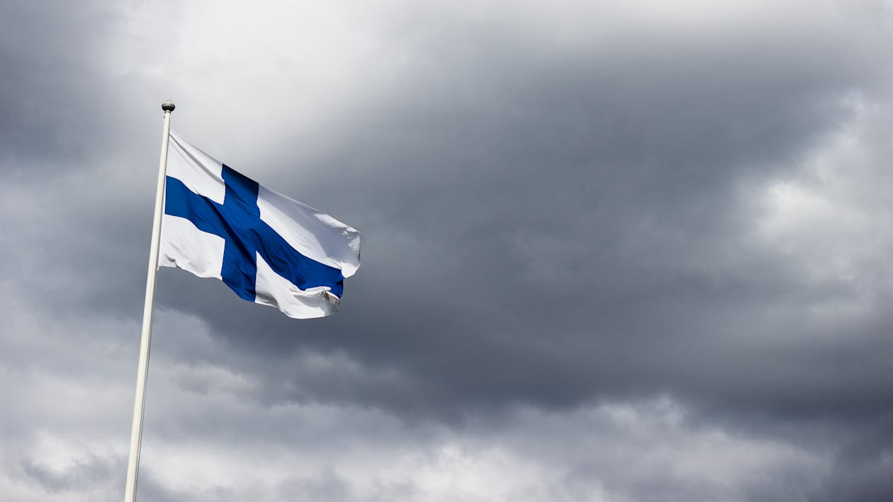 Finland’s national flag waving on a pole, symbolizing its top spot in the world happiness report.