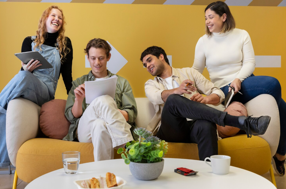Young coworkers collaborating in a relaxed lounge during a hybrid meeting, showcasing Gen Z work culture.