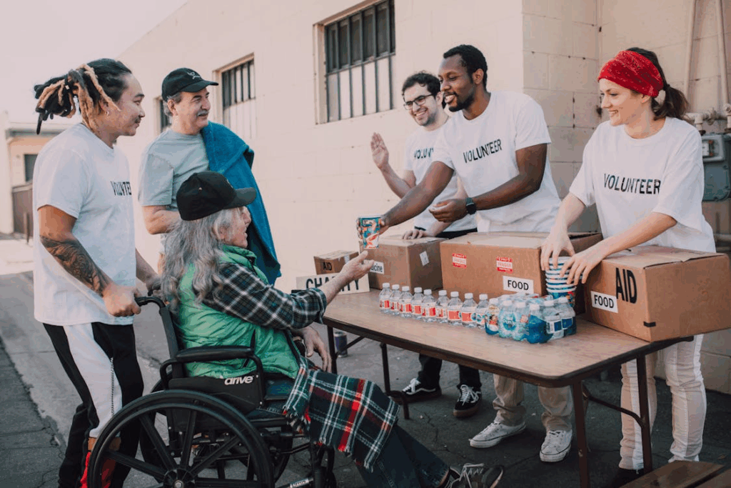 Volunteers giving food and water to a person in a wheelchair, illustrating the health benefits of kindness through connection.